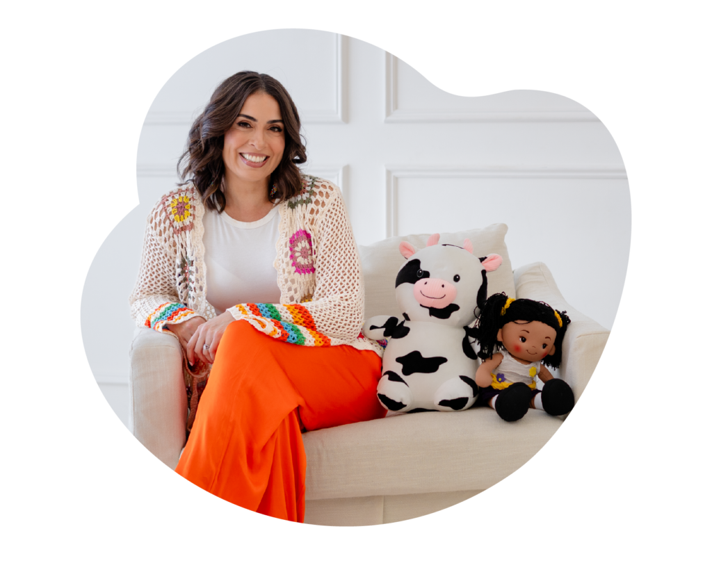 woman in orange pants on chair next to a stuffed animal cow and doll